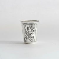 Silver cup with intricate black floral patterns on a white background