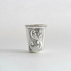 Silver cup with intricate black floral patterns on a white background