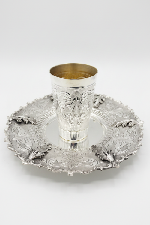 Silver kiddush cup with intricate design on a matching tray