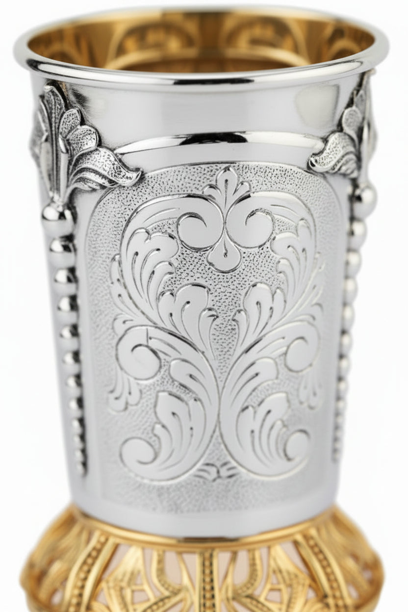 Silver and gold kiddush cup with ornate design on a white background