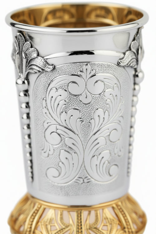 Silver and gold kiddush cup with ornate design on a white background