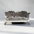 Decorative silver napkin holder box with intricate designs on a light gray background