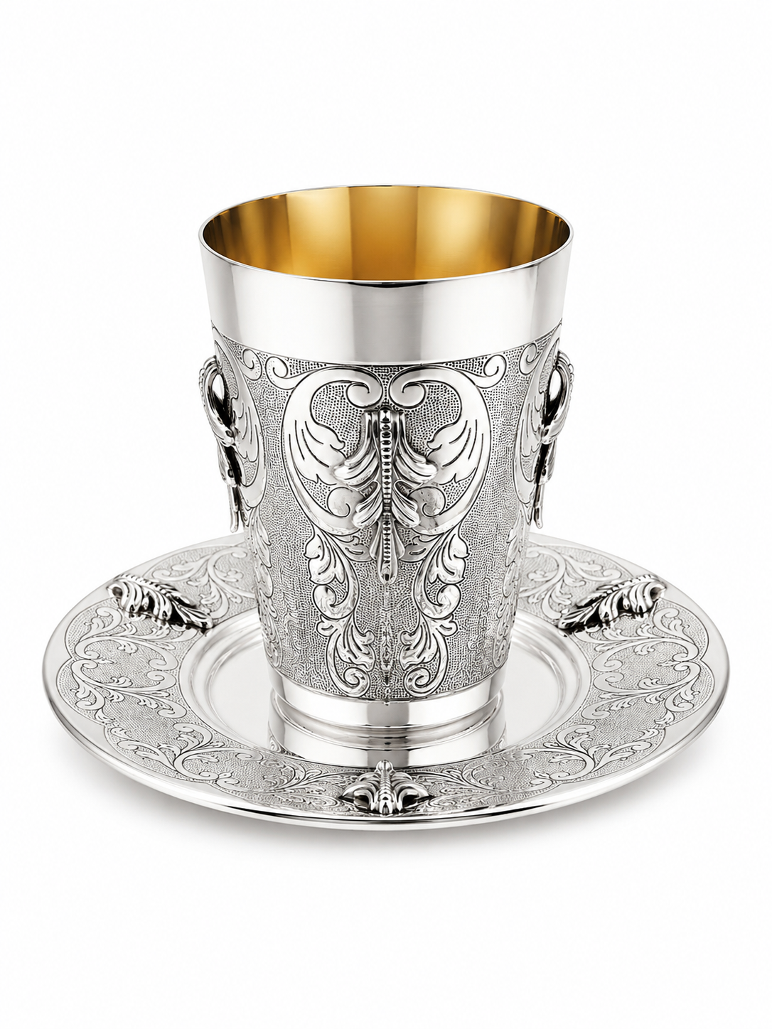 An ornate sterling silver Kiddush cup with a gold interior, featuring intricate floral engravings and side handles, shown on a matching engraved silver saucer by hadad bros silverware
