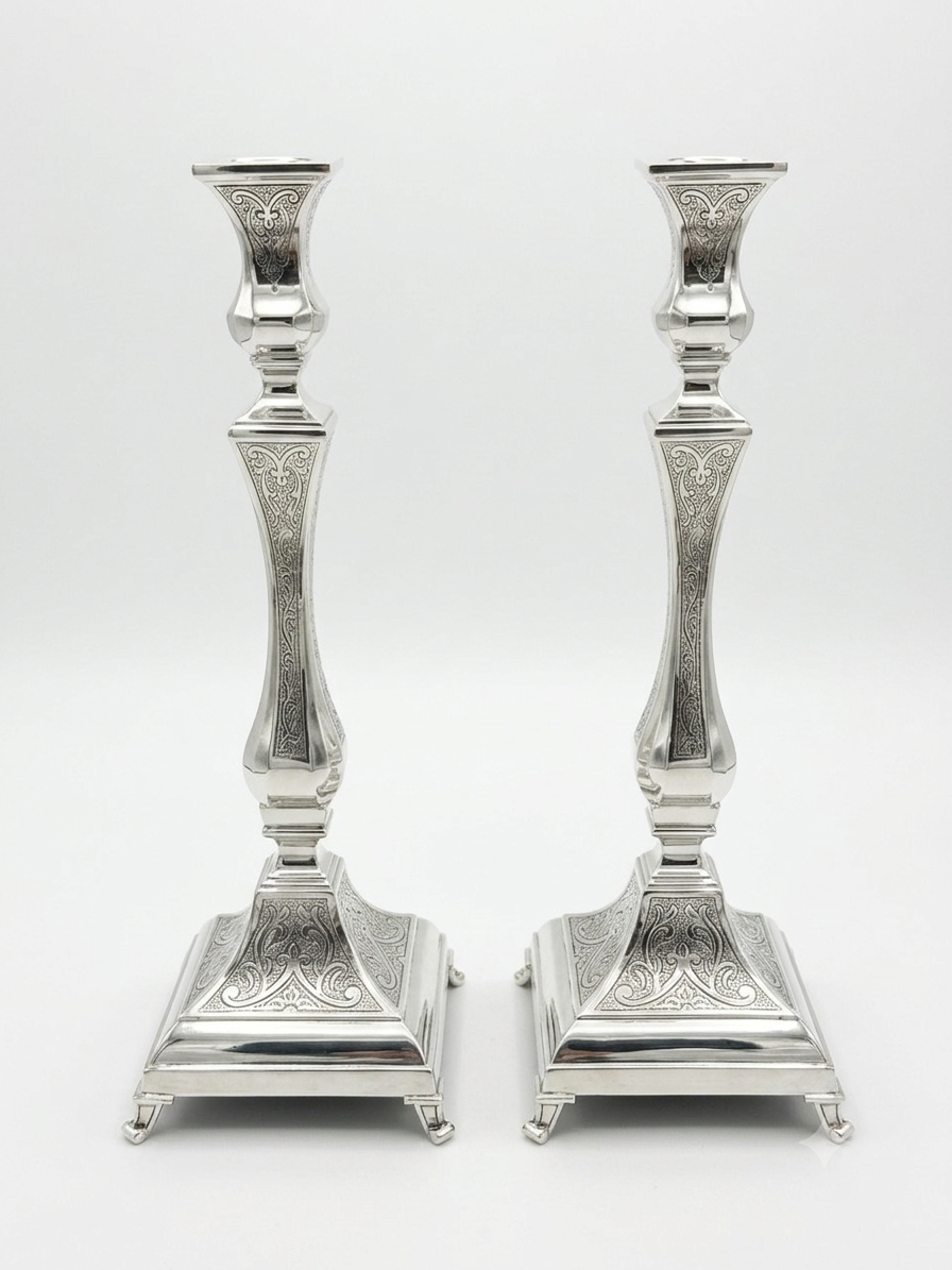 Pair of silver candlesticks with intricate designs on a white background