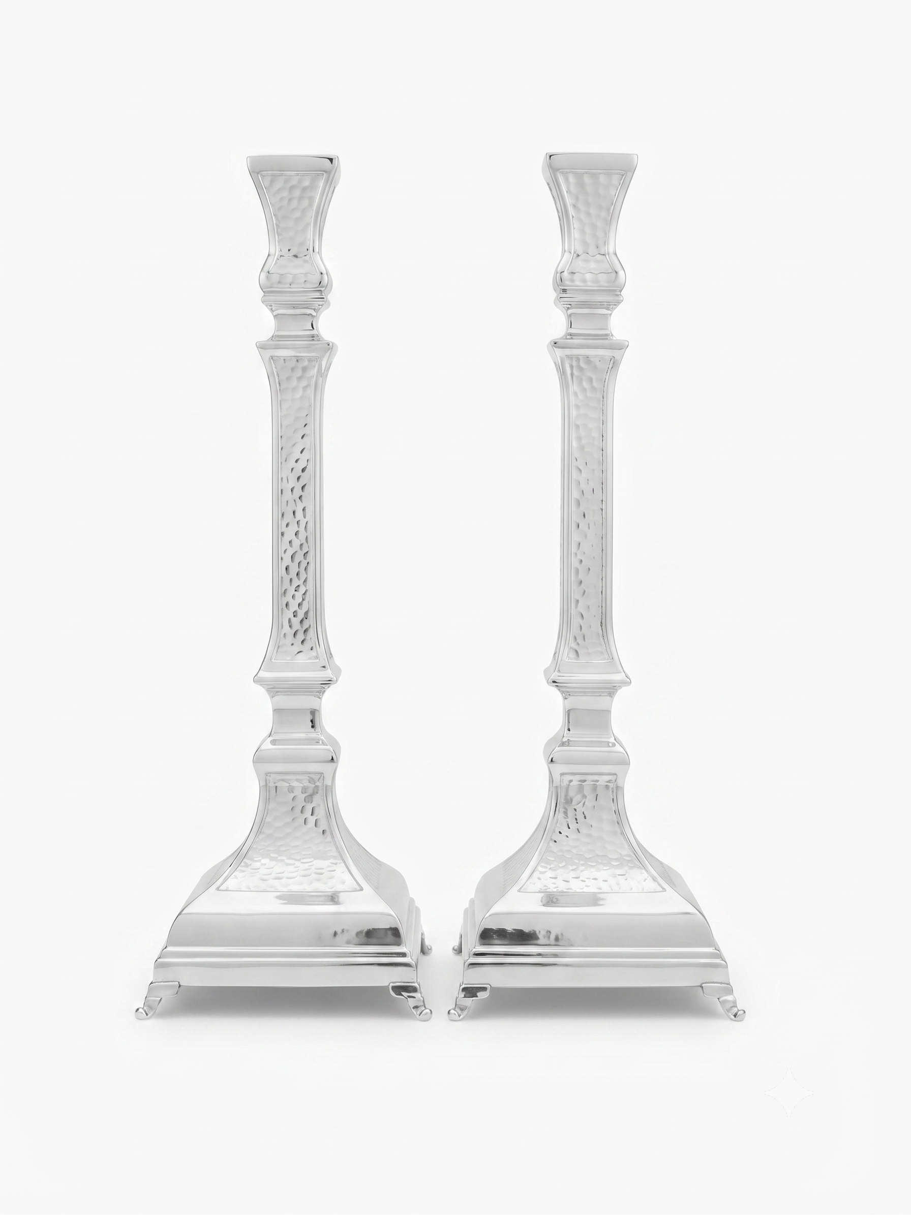 A pair of ornate silver candlesticks with detailed textured engravings and flared bases, shown against a plain white background. hammered silver candlesticks by hadad bros silverware