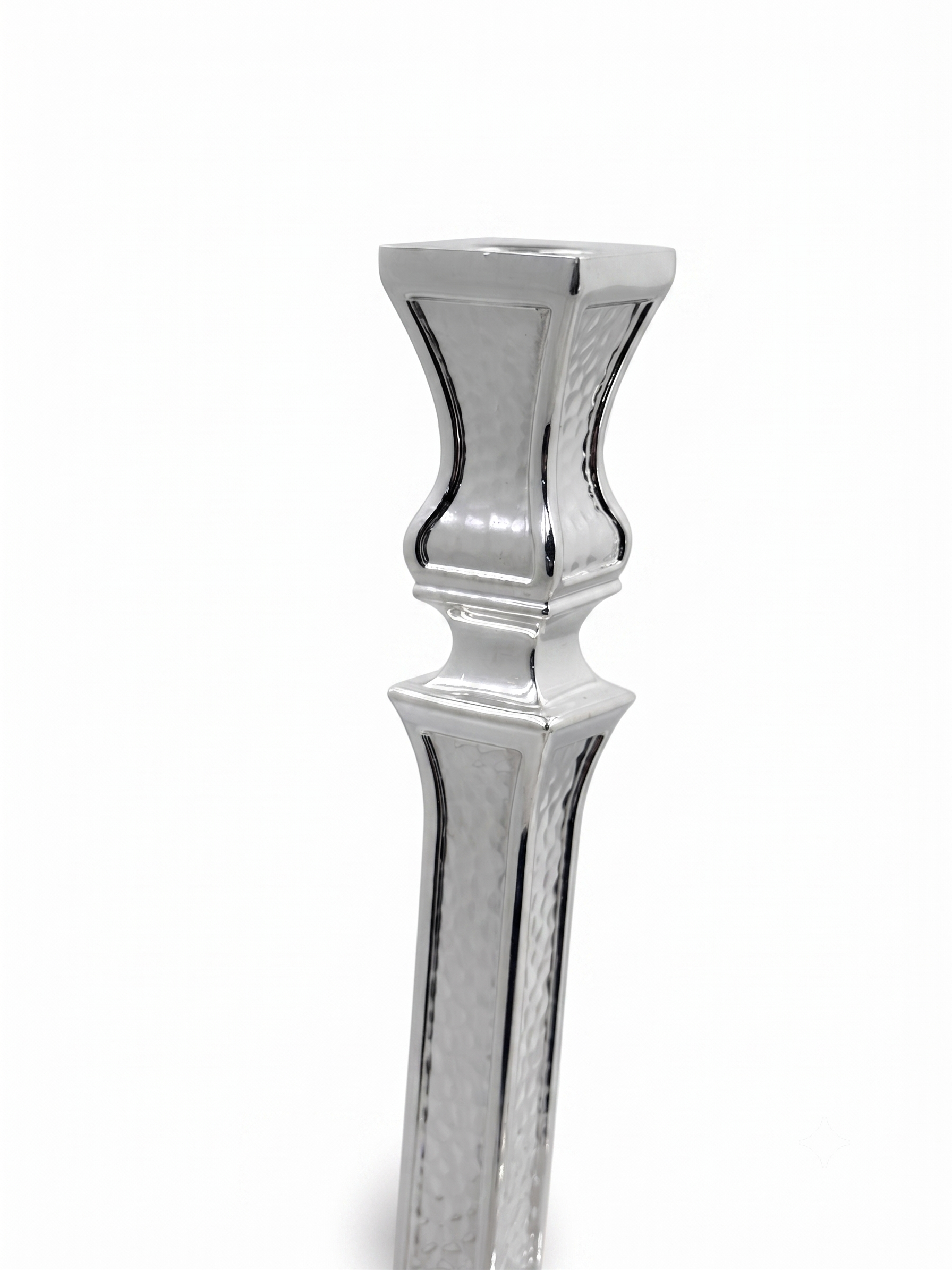 A pair of ornate silver candlesticks with detailed textured engravings and flared bases, shown against a plain white background. hammered silver candlesticks by hadad bros silverware