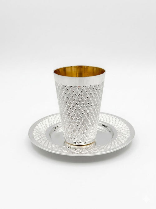 Silver kiddush cup with gold interior and diamonds pattern on a matching tray against a white background