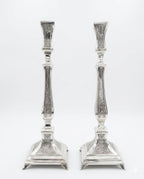 Pair of silver candlesticks with intricate designs on a white background