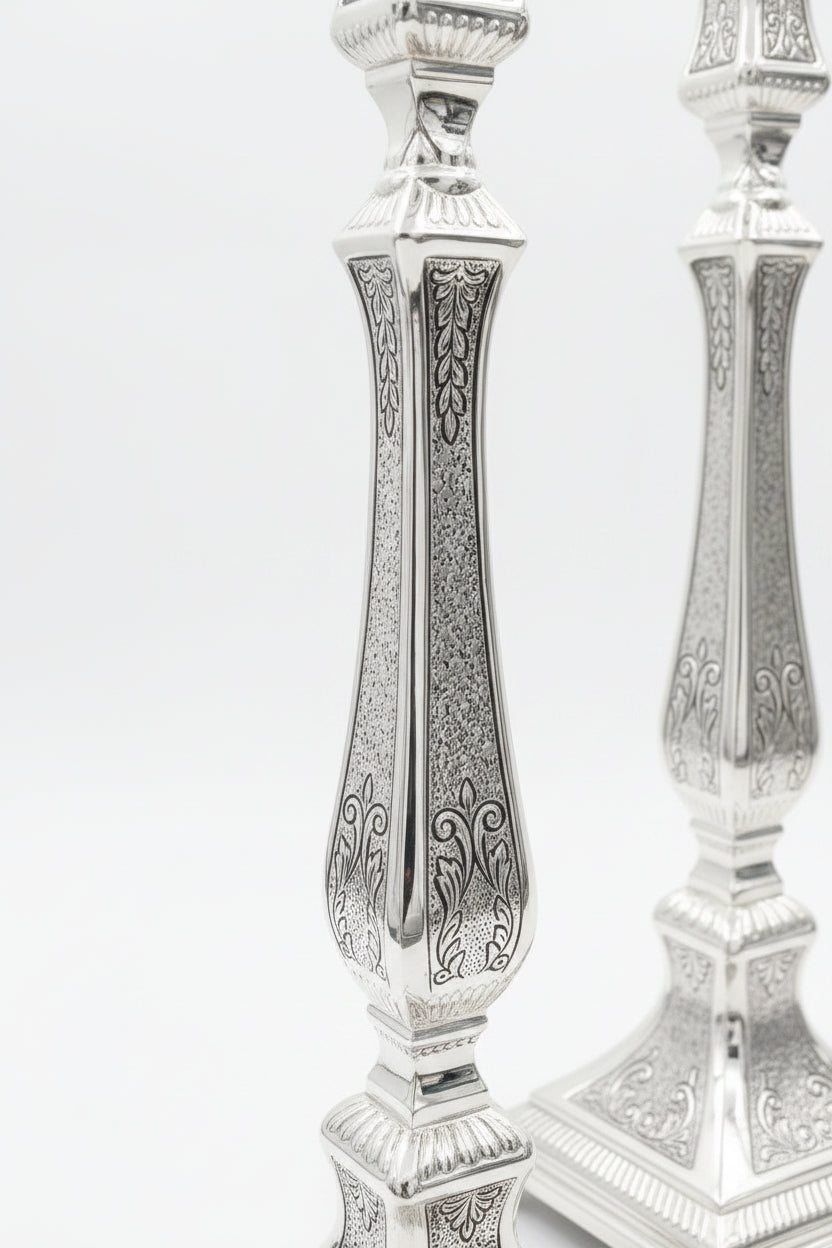 Pair of silver candlesticks with intricate designs on a white background