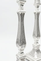 Pair of silver candlesticks with intricate designs on a white background