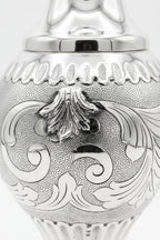 Silver decorative bottle with intricate designs on a white background