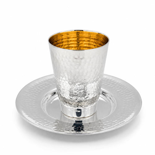 A silver hammered kiddush cup with a gold interior, shown on a matching silver hammered plate by hadad bros silverware