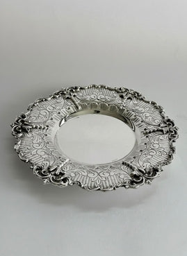 Silver kiddush cup with intricate designs on a matching saucer against a white background