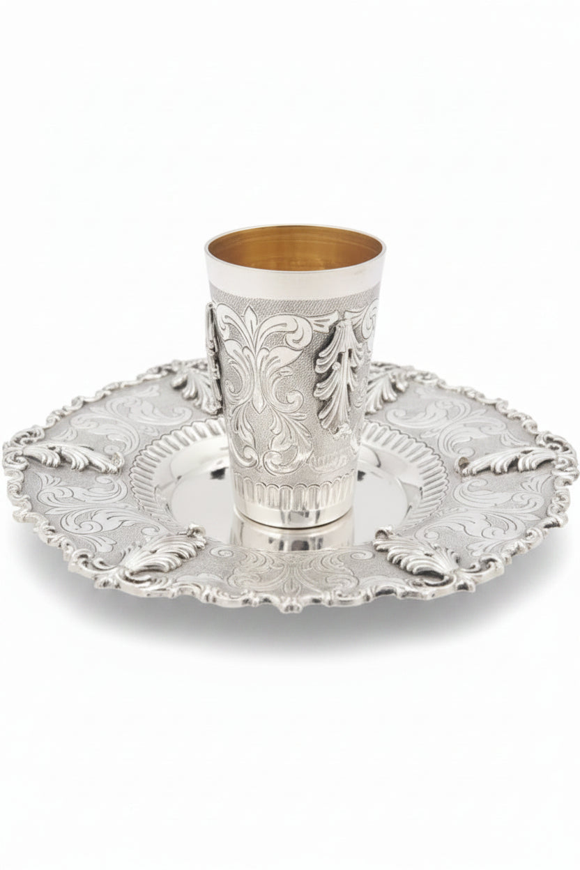 Silver kiddush cup with gold interior on an ornate silver tray against a white background