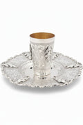 Silver kiddush cup with gold interior on an ornate silver tray against a white background