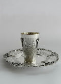 Silver kiddush cup with intricate designs on a matching saucer against a white background