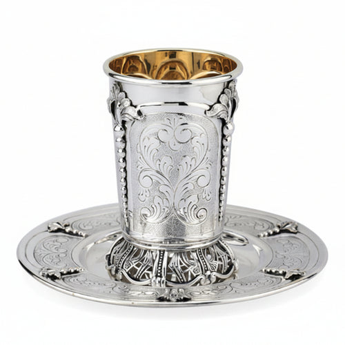 Silver kiddush cup with gold interior on a matching tray against a white background