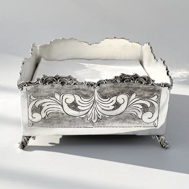 Decorative silver napkin holder box with intricate designs on a light gray background