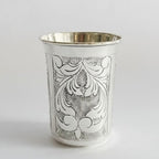 Silver cup with intricate black floral patterns on a white background