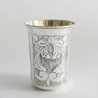 Silver cup with intricate black floral patterns on a white background